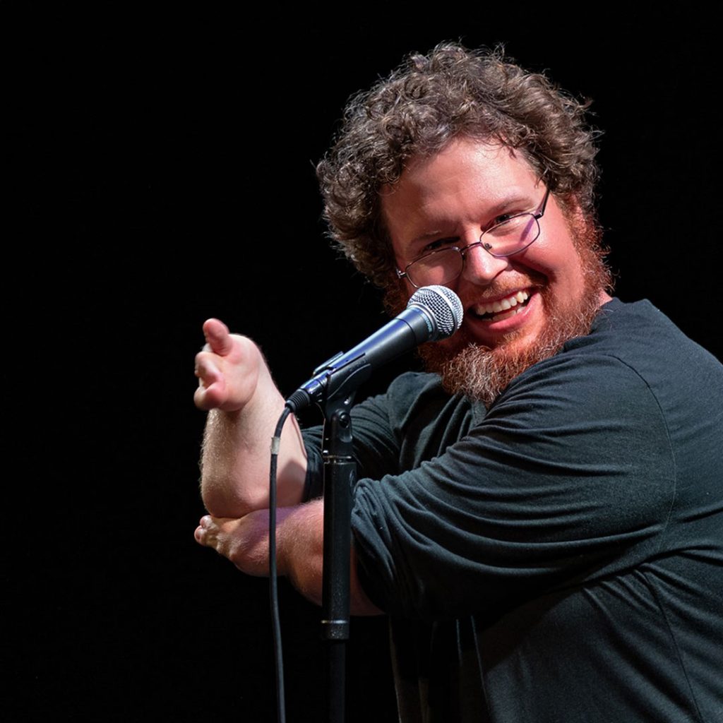 Ryan Niemiller at a microphone on stage doing a comedy act.