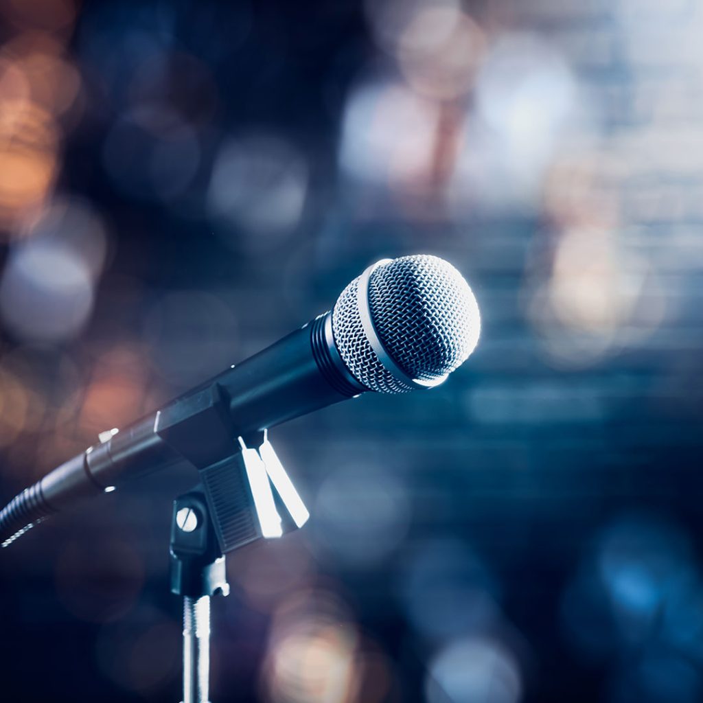 Microphone on a stand-up comedy stage with colorful bokeh.