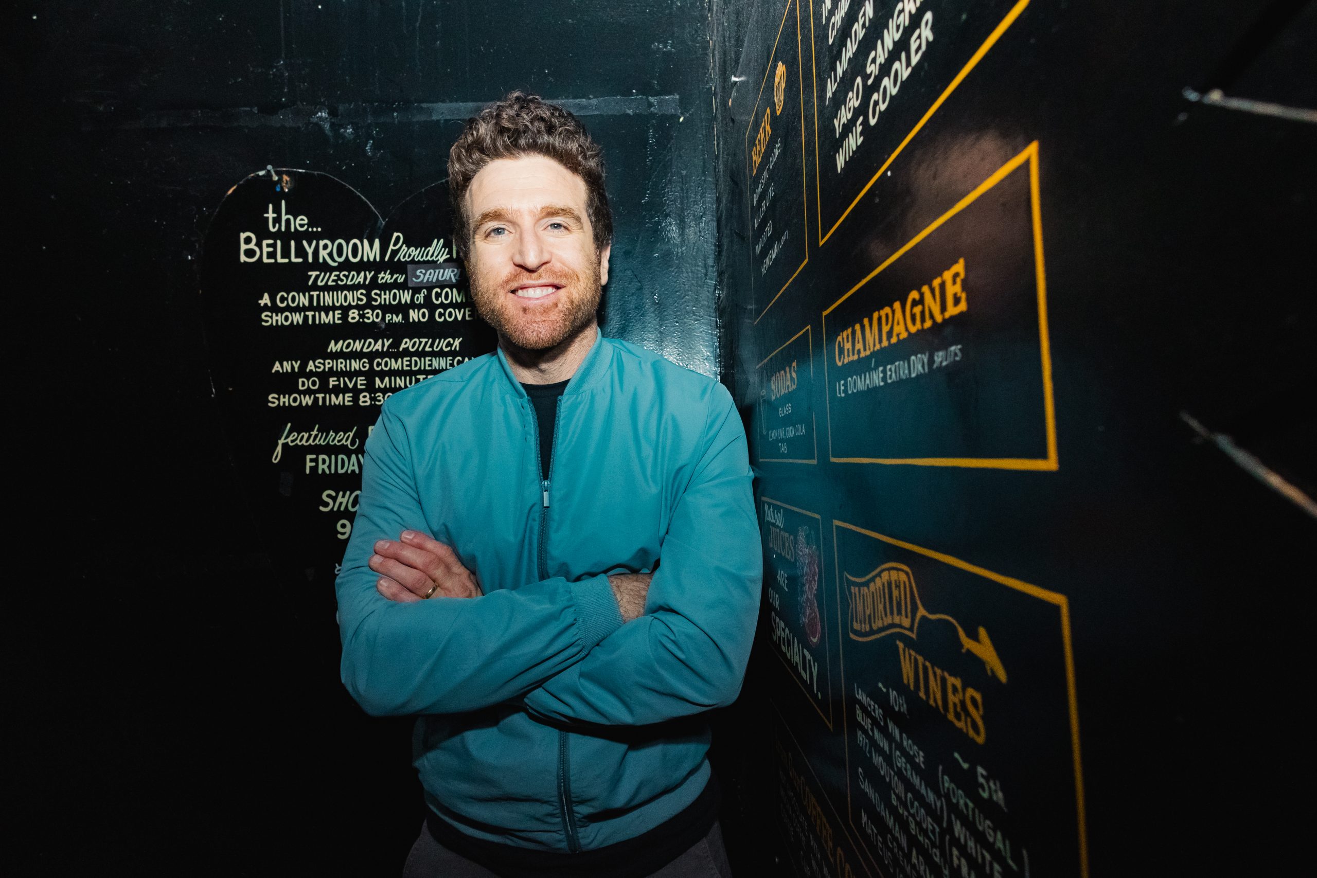 Mo Mandel who is associated with SF Comedy Competition posing behind a menu of beverages.